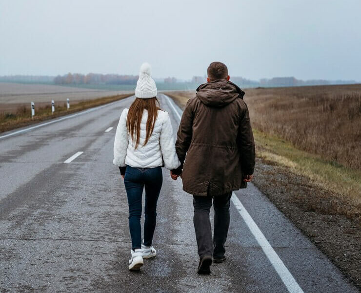 Back view of couple holding hands on the road