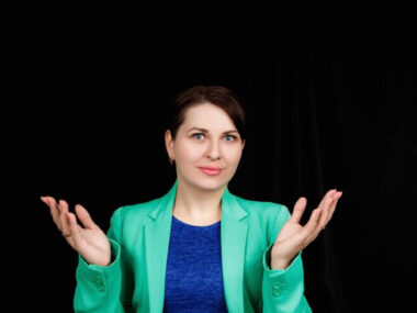 Studio close up portrait of a girl of Slavic appearance worn a blue blouse and a blue-green jacket on a black space.