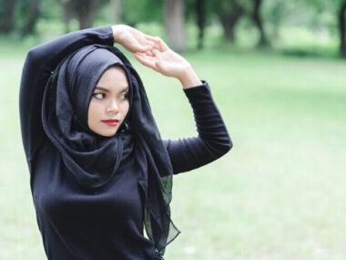 Beautiful young muslim asian woman doing exercise before running over blurred the green field