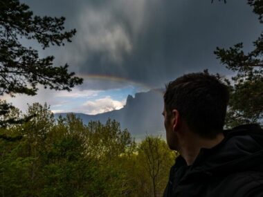Man looking at rainbow by mountain against cloudy sky