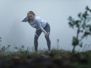 Tired athletic woman taking a break while being out of breath after the run during misty morning