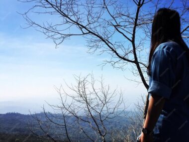 Woman standing by bare tree against sky