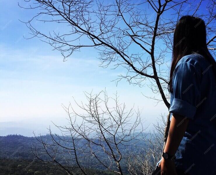 Woman standing by bare tree against sky