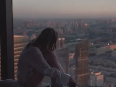 Woman Sitting by Window over City at Dusk