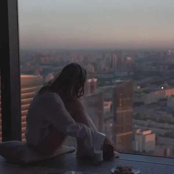 Woman Sitting by Window over City at Dusk