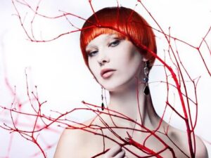 Young beautiful woman with red hair between red branches