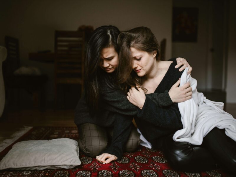 Woman Hugging and Comforting her sad Friend while Sitting on the Floor